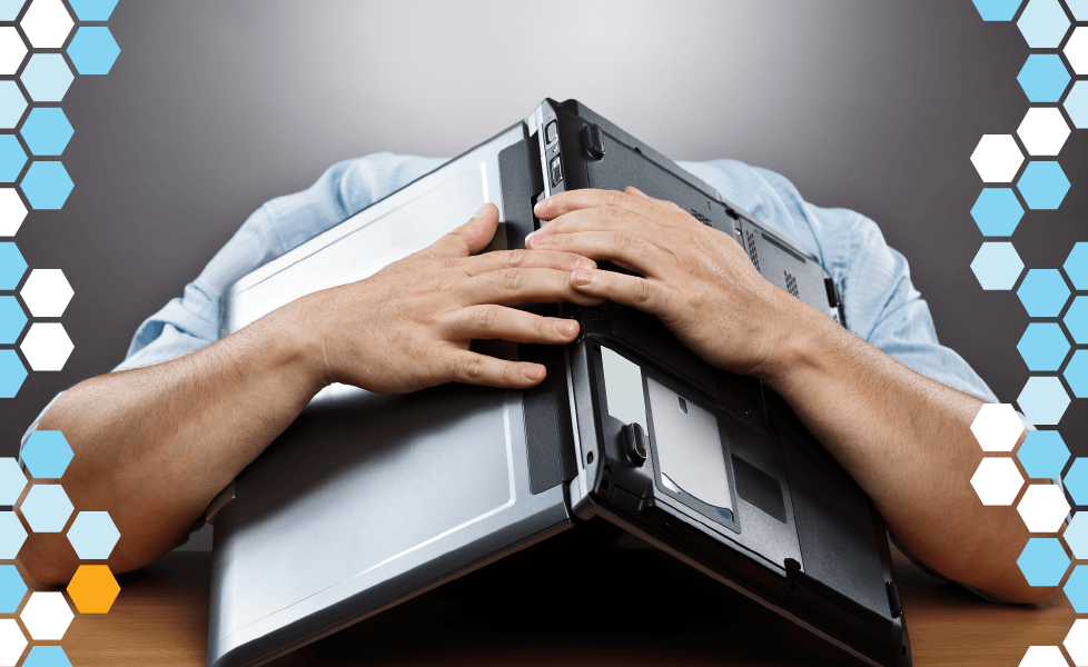 A frustrated man has a computer over his head with his forehead on his desk.